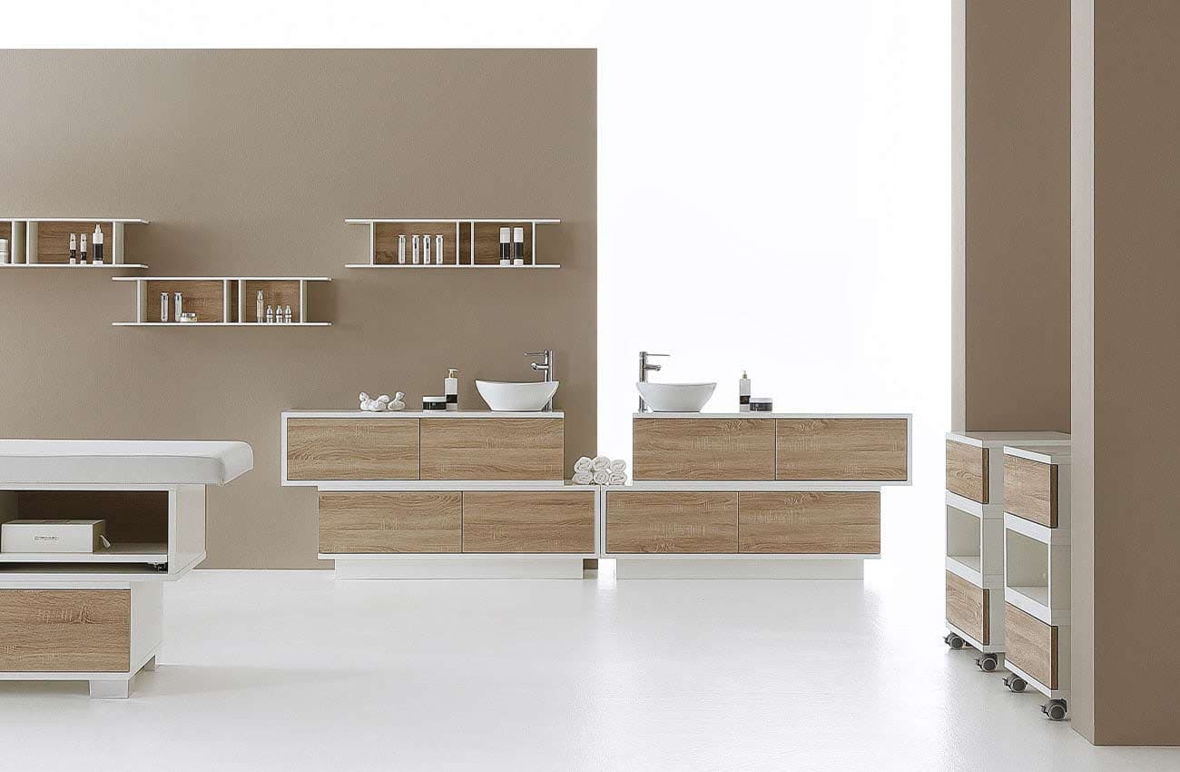Cabina estetica Vismara con mobili lavabo in legno chiaro e bianco, mensole a parete e lettino